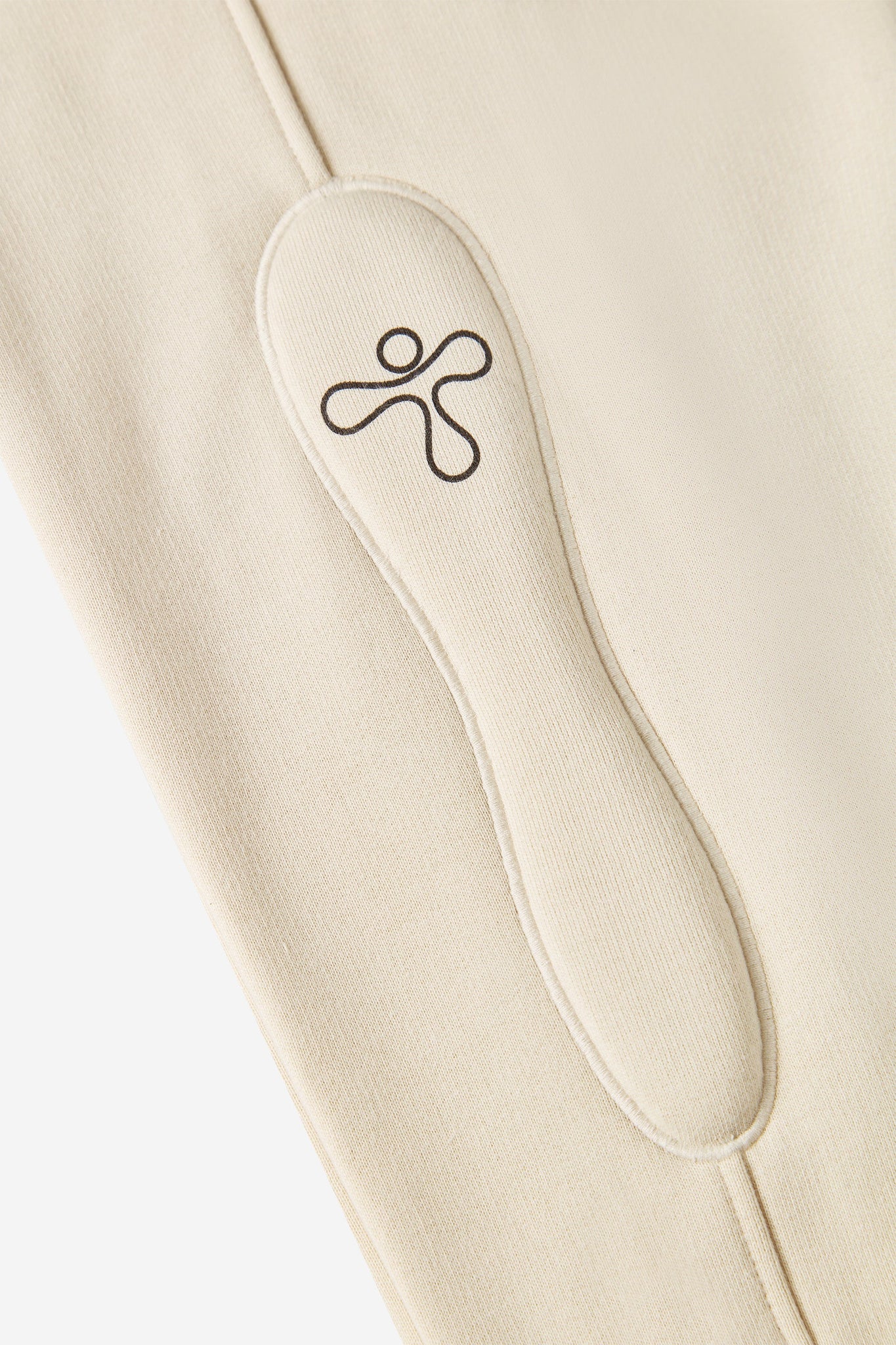 alt="detail of beige track pants with padded embroidered detail and print"