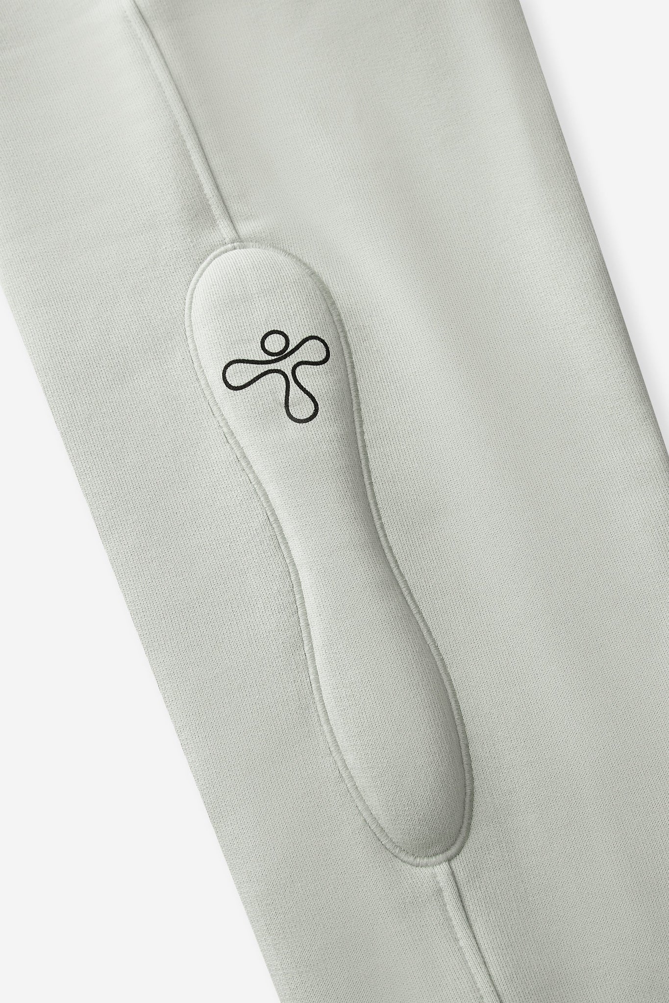 alt="detail of light green jogger pants with padded embroidered detail and print"